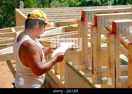 Latin work crew building wooden stick built house home cutting measure nailing on hot day Stock Photo