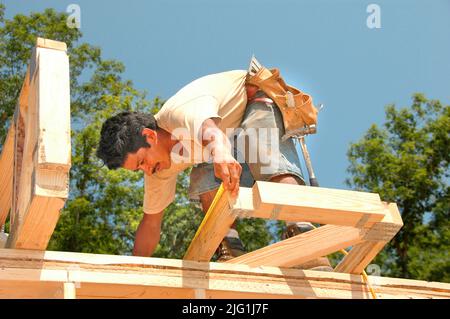 Latin work crew building wooden stick built house home cutting measure nailing on hot day Stock Photo