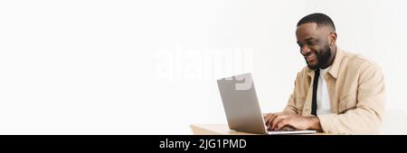 Web banner. Smiling professional black business man using laptop computer working from home office. Happy afro american freelancer man working at home Stock Photo