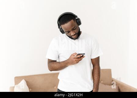 Portrait of an african american young guy enjoying listening to good music at home, looking at the smartphone screen Stock Photo
