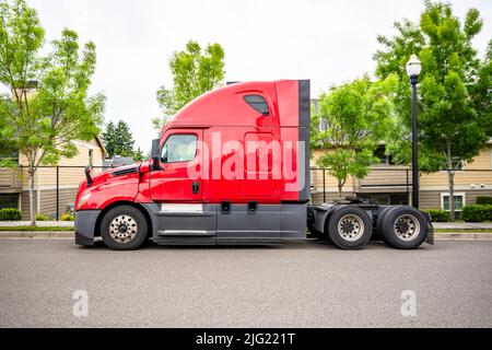 Red industrial big rig semi truck with truck driver cab sleep compartment and with lubricated fifth wheel without semi trailer standing on the city st Stock Photo
