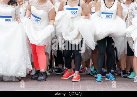 Crowd of brides prepares for their race by lining up in front of starting line, in which groom will serve as their goal. It's a Start of Love Story. Stock Photo