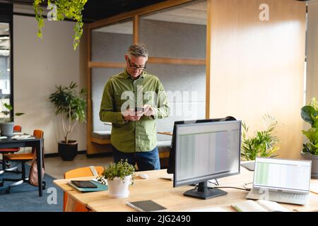 Caucasian mature businessman using smart phone in creative office Stock Photo