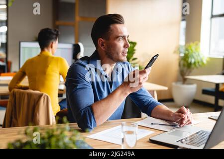 Caucasian young businessman talking on smartphone in creative office Stock Photo