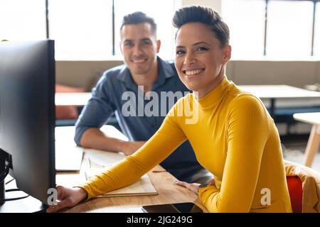 Portrait of smiling multiracial colleagues sitting at desk in creative office Stock Photo