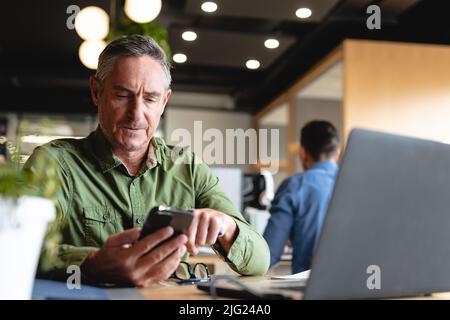 Caucasian mature businessman using smart phone at desk in creative office Stock Photo