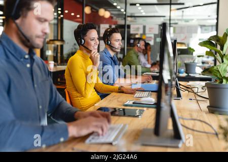 Smiling caucasian female customer service executive talking through headset in office Stock Photo