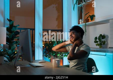 Young tired overworked african american woman freelancer in eyeglasses working late from home Stock Photo