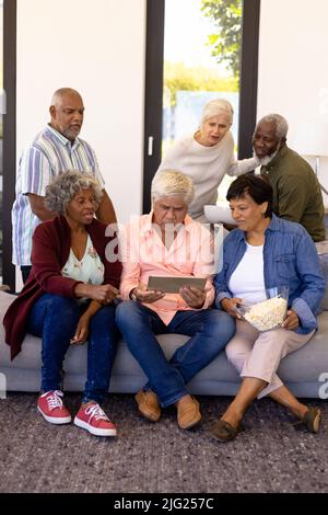 Multiracial senior friends with popcorns watching match over digital tablet in nursing home Stock Photo