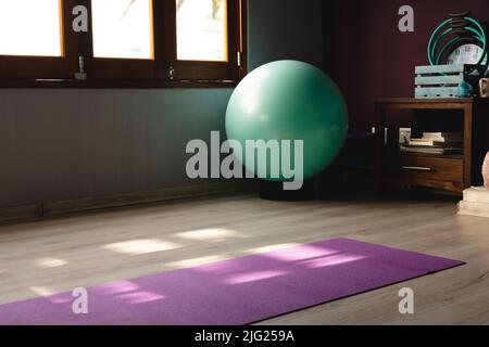 Fitness ball and exercise mat on hardwood floor in empty room at home, copy space Stock Photo