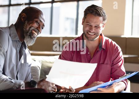 Happy multiracial male business colleagues discussing over documents in creative office Stock Photo