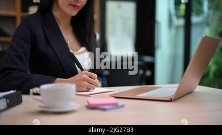 An attractive asian female secretary or office worker working at her desk, taking notes on the notebook. cropped image Stock Photo