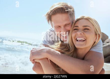 A young loving couple enjoying a day at the beach while smiling hugging and having fun, showing affection at the ocean. Romantic couple cuddling and Stock Photo