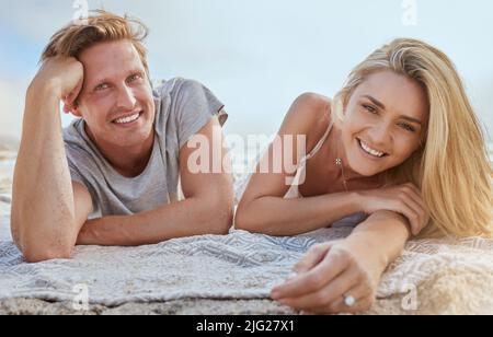 Portrait of happy young couple lying on blanket and enjoying beach vacation. Smiling young blonde man and woman relaxing on shore and enjoying their Stock Photo