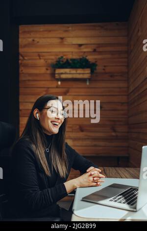 businesswoman smiling happily during an online meeting in a modern co-working space. Cheerful female entrepreneur communicating with her business asso Stock Photo