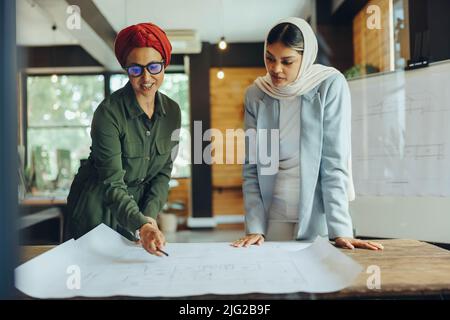 Muslim architects working on blueprint drawings in a modern office. Two creative businesswomen planning a new innovative project. Female designers wea Stock Photo