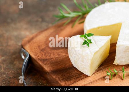 Sliced Camembert Cheese with thyme on wood plate. Camembert is a moist, soft, creamy, surface-ripened cow's milk cheese. Stock Photo