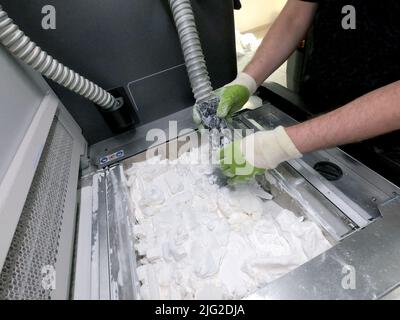 A man working with a working vacuum cleaner to clean the white powder of polyamide from a model printed on a 3D printer inside a 3D printer. Cleaning objects printed on an industrial powder 3D printer Stock Photo