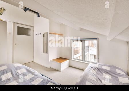 Comfortable beds without ornamental blanket placed near glass door with rack in light bedroom Stock Photo