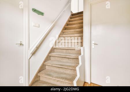 Closed white door of room located near framed pictures and stylish lamp on top of stairway at home Stock Photo