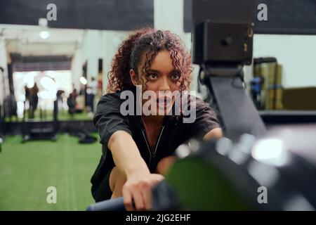 African American female using a rowing machine during cross fit training. Female athlete exercising intensely in the gym. High quality photo Stock Photo