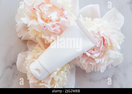 Flat lay composition with cosmetic products and peony flowers on a marble. Top view. Unbranded plastic white tube Stock Photo