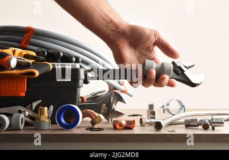 Plumber toolbox with material on wooden table and hand picking accessories with isolated background. Front view. Horizontal composition. Stock Photo