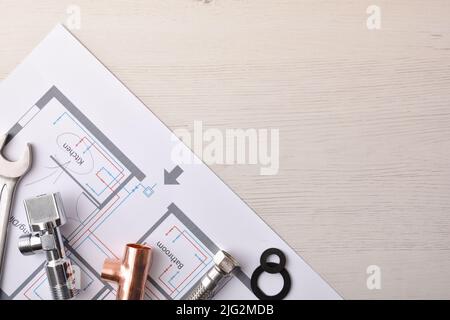 Conceptual background of elements of water installation in housing with plans and plumbing material on white wooden office table. Top view. Horizontal Stock Photo