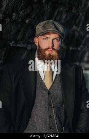 Bearded man with blue eyes  wearing  vintage clothes from the 20s with a brick background Stock Photo