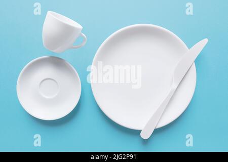 White coffee cup and dish with knife, isolated on light blue Stock Photo