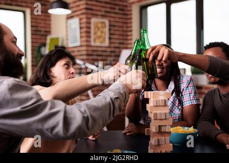 Multiethnic happy group of friends celebrating reunion at home while playing society games together. Multiracial people sitting in living room while enjoying snacks, beverages and leisure activity. Stock Photo