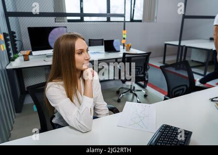 Attractive friendly young businesswoman sitting at the table in office. Stock Photo