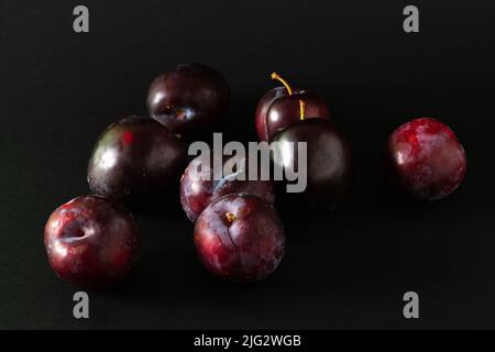 Stack of purple plums on black background. Stock Photo