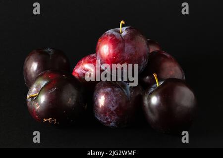 Stack of purple plums on black background. Stock Photo