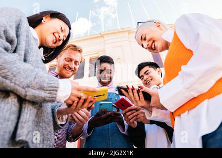 Five cherful friends using his cellphone and having fun together. Low angle of multiethnic group of happy people sharing media. Stock Photo