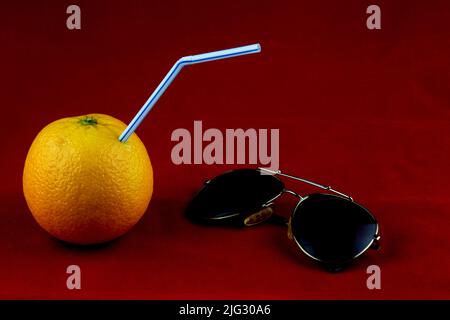 Orange and drinking straw for orange drink with sunglasses isolated on red Stock Photo