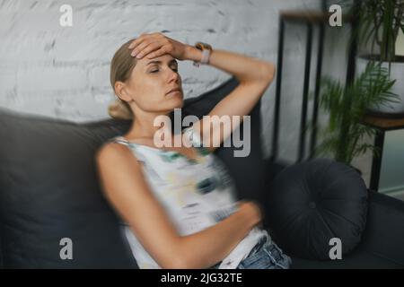 woman having migraine headache at home. sitting on couch with hand on forehead Stock Photo