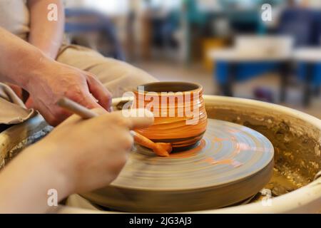 The Potter with student coloring a pot from clay on a Potter's wheel at workshop. Teaching pottery on a potter's wheel. Hobbies, craft and handwork. H Stock Photo