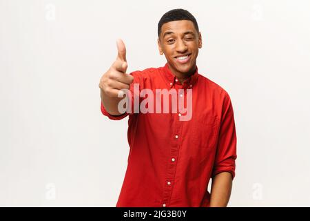 Portrait of man wearing red casual style shirt, pointing finger pistols to camera playfully and flirting, choosing lucky winner. Indoor studio shot isolated on white background Stock Photo