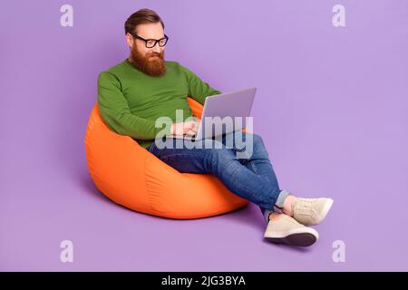 Full body photo of handsome intelligent guy sitting bag use wireless netbook isolated on violet color background Stock Photo