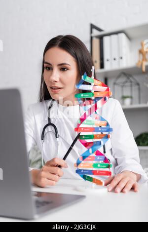 Doctor pointing at dna model during video call on laptop in hospital Stock Photo