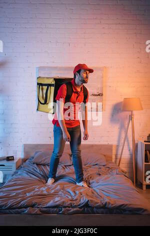 Deliveryman in uniform standing on bed while suffering from sleepwalking at night Stock Photo