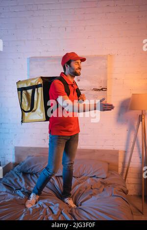 Smiling deliveryman outstretching hand while suffering from sleepwalking on bed Stock Photo