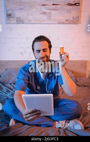 Confused doctor holding pills and digital tablet while suffering from sleepwalking on bed Stock Photo