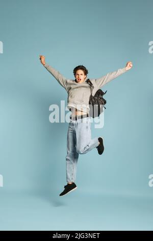 Happy student in jeans and grey hoodie jumping isolated over blue background. Concept of emotions, facial expression, youth. Back to school Stock Photo