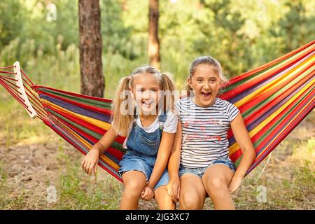 Kids relax in colorful rainbow hammock. cation. Children relaxing. Stock Photo