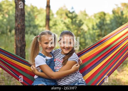 Kid girls relax in colorful rainbow hammock. Stock Photo