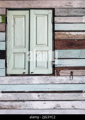 Old grunged wooden window frame painted white vintage with old colourful plywood wall. Antique window frame and old panes. Old closed window and plank Stock Photo