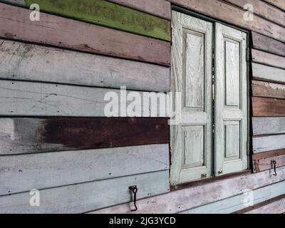 Old grunged wooden window frame painted white vintage with old colourful plywood wall. Antique window frame and old panes. Old closed window and plank Stock Photo