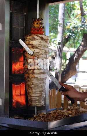 A chicken shawarma skewer roasting on a rotating pole. Stock Photo